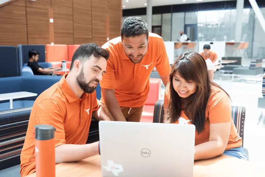 Three UT students collaborating on a laptop computer